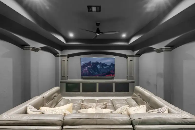 Home theater with a tan leather sectional, a television in a built-in cabinet, and a tray ceiling.