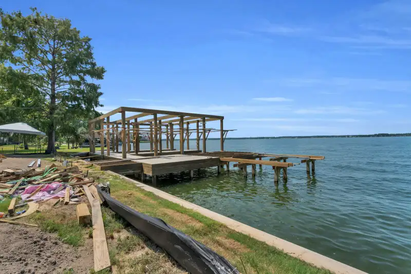 Dock frame under construction at the lakefront, with timber pilings and the shoreline beside it.