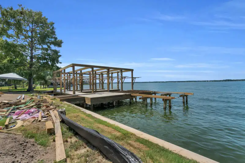 Dock frame under construction at the lakefront, with timber pilings and the shoreline beside it.