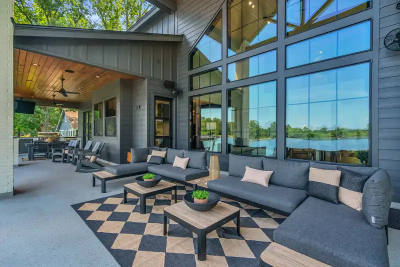 Outdoor living area with gray sectional seating, a checkered rug, and a wood-paneled ceiling.