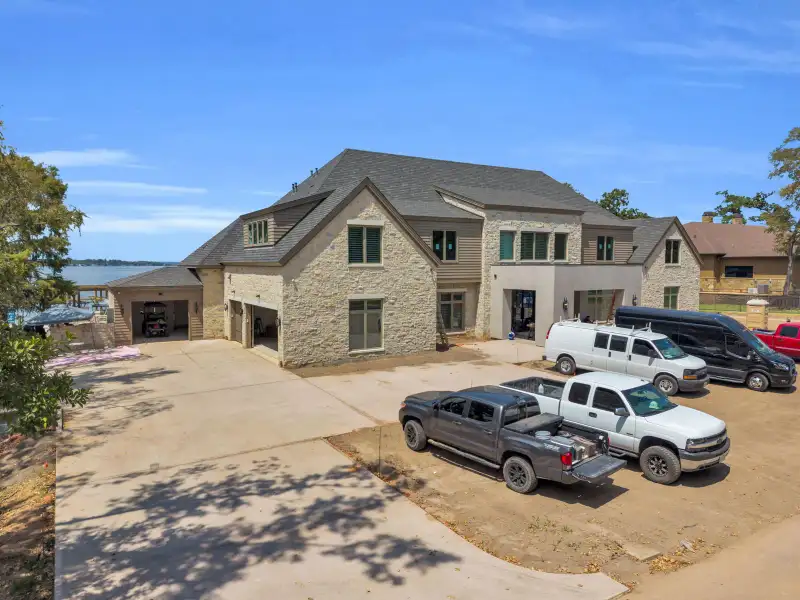 Aerial view of the Escondido home's stone facade and garage bays, with a lake in the background.