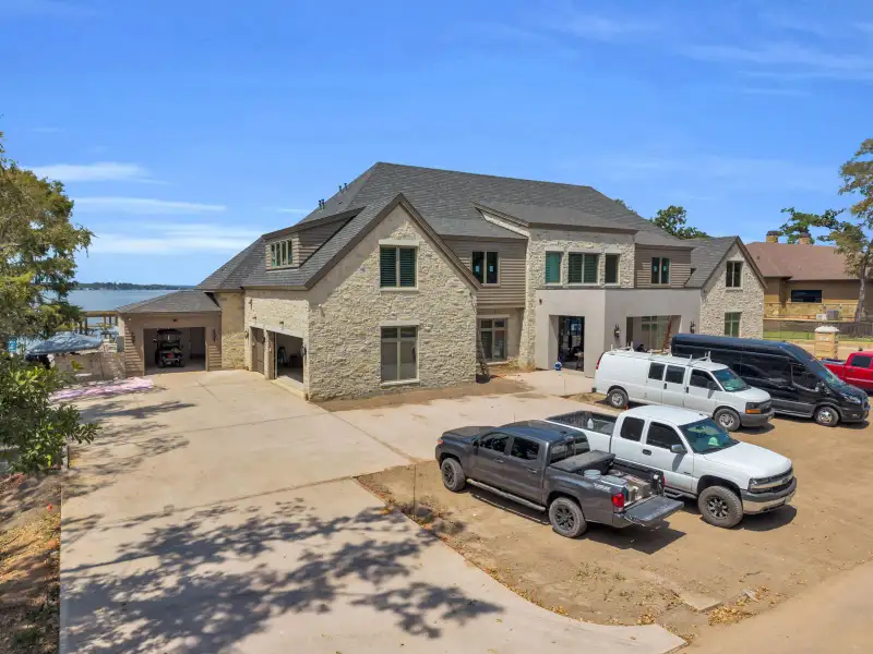 Aerial view of the Escondido home's stone facade and garage bays, with a lake in the background.