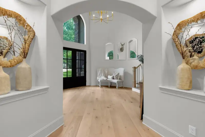 Entry hall with an arched opening, black French doors, a bench, and a brass chandelier.