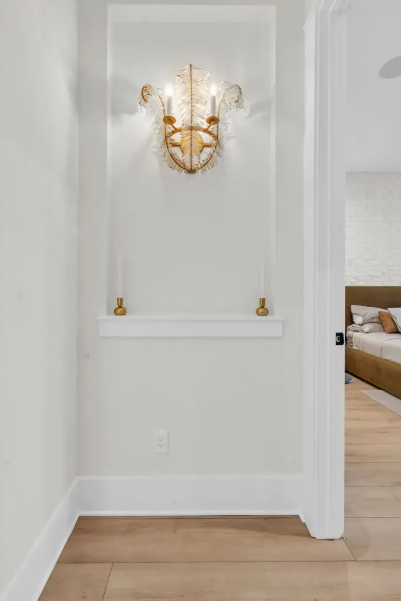 Hallway niche with a gold crystal wall sconce above a white shelf, beside a doorway to a bedroom.