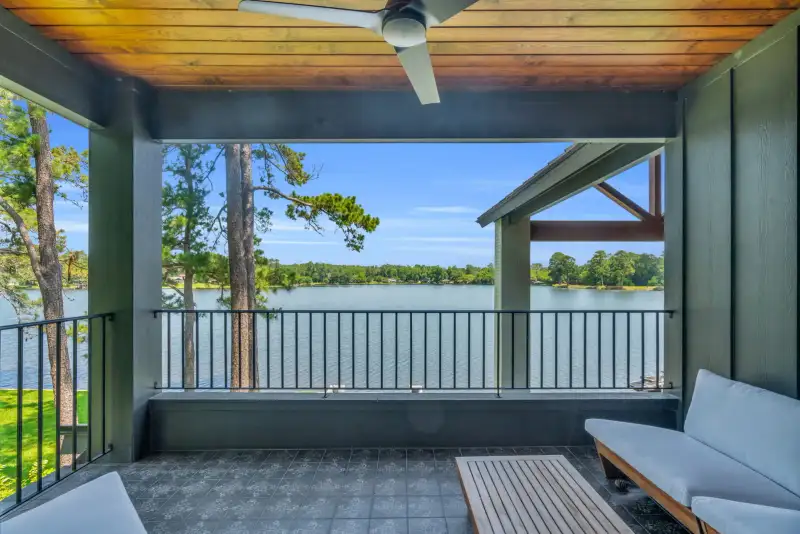 Covered balcony with a wood ceiling, black railings, and a view of water through the trees.