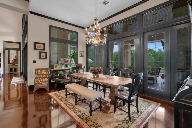 Dining room with a wood table, a crystal chandelier, and a sign beside black French doors.