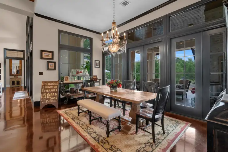 Dining room with a wood table, a crystal chandelier, and a sign beside black French doors.