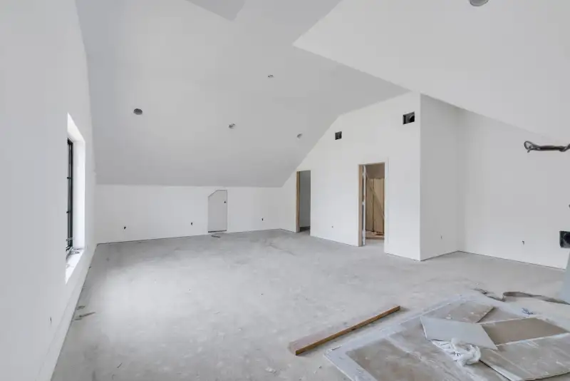 Vaulted unfinished room with white walls, a tall side window, and a concrete floor.