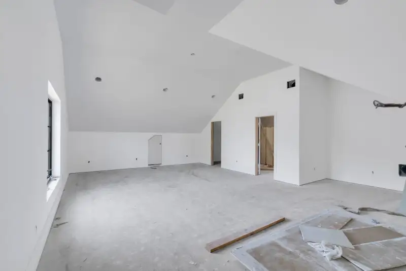 Vaulted unfinished room with white walls, a tall side window, and a concrete floor.