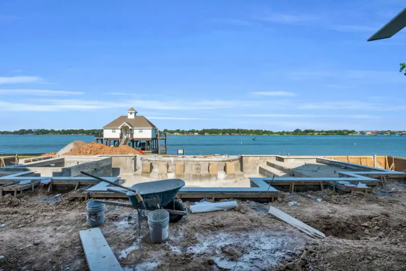 Construction foundation on a lake shore with an elevated house on pilings in the background.