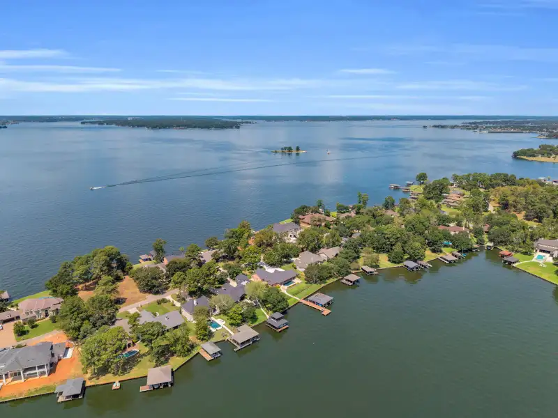 Aerial view of lakeshore homes along a point, with boat docks and a wooded far shoreline.