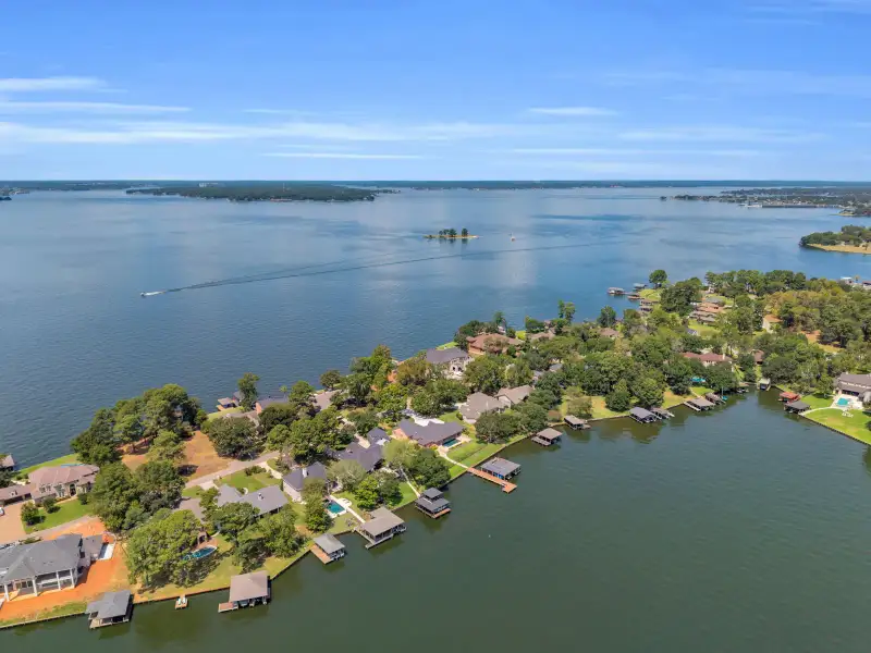 Aerial view of lakeshore homes along a point, with boat docks and a wooded far shoreline.