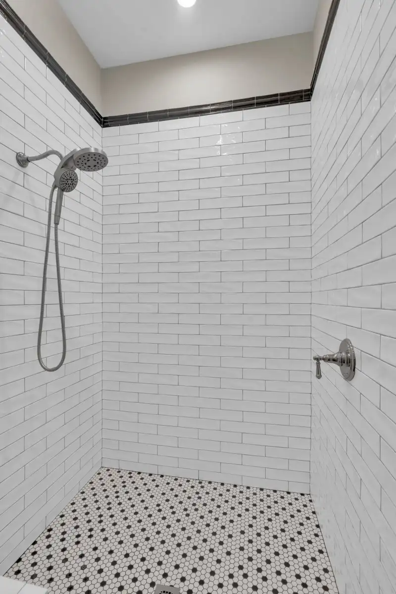 Shower with white subway tile walls, a black-and-white patterned tile floor, and a handheld showerhead.