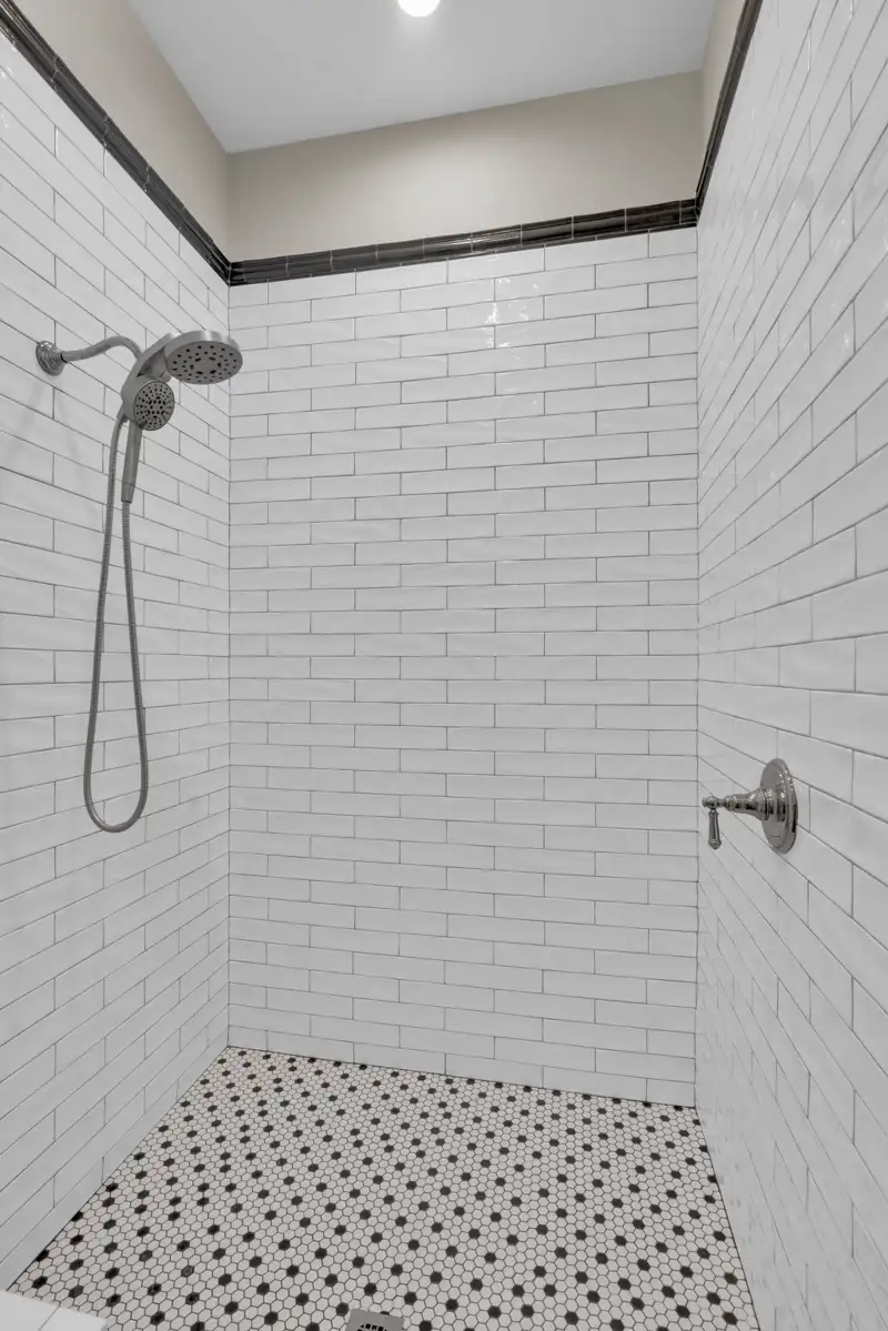 Shower with white subway tile walls, a black-and-white patterned tile floor, and a handheld showerhead.
