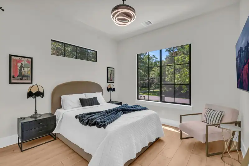 Bedroom with an upholstered headboard, a pink accent chair, and a black-framed window.