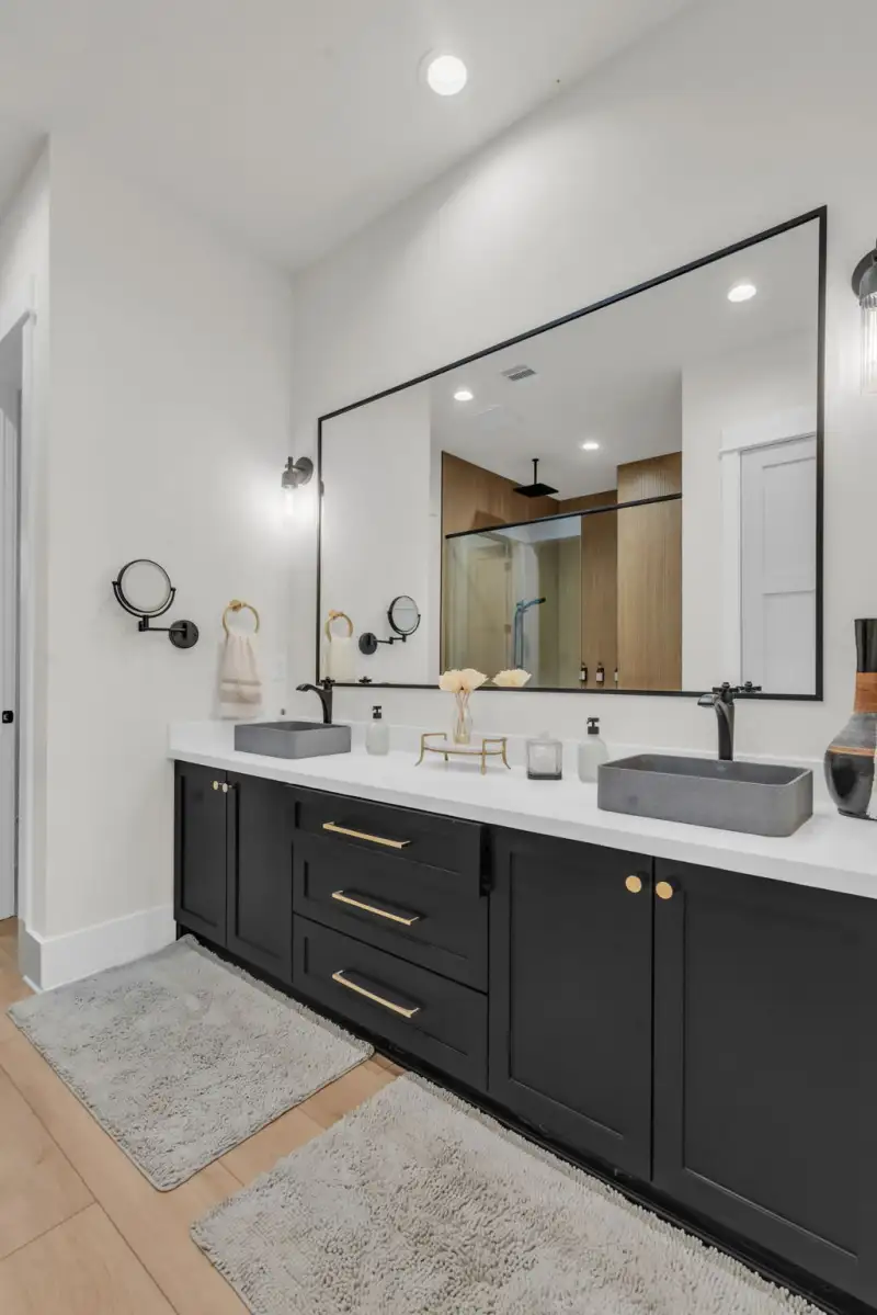 Double vanity with black cabinets, gray vessel sinks, a black-framed mirror, and gold hardware.