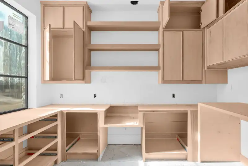 Unfinished kitchen with light wood wall and base cabinets, open shelves, and a black-framed window at left.