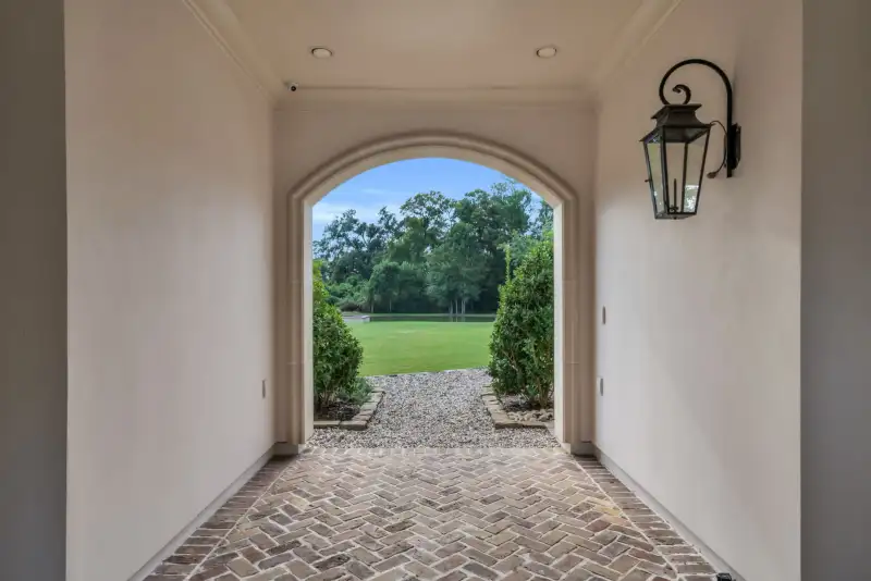 Arched covered passage with a brick herringbone floor, wall lantern, and a view of the lawn.