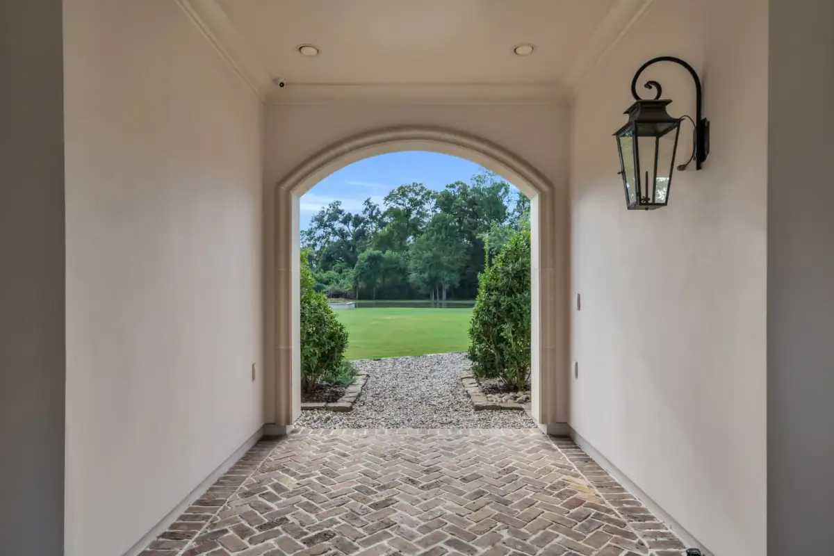 Arched covered passage with a brick herringbone floor, wall lantern, and a view of the lawn.