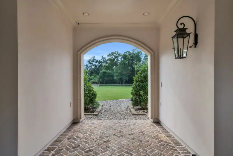 Arched covered passage with a brick herringbone floor, wall lantern, and a view of the lawn.