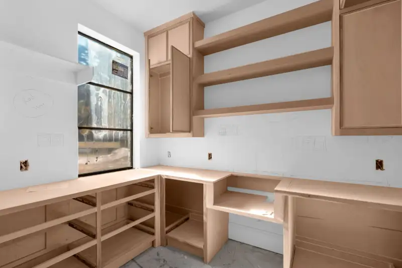 Unfinished room with light wood cabinets along an L-shaped counter and a black-framed window at left.