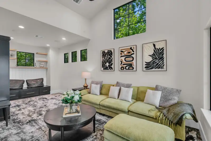 Bonus room with a green sectional, framed wall art, and black-framed windows.