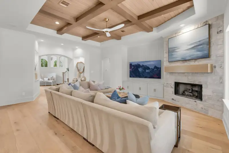 Living room with a wood plank coffered ceiling, a ceiling fan, a stone fireplace, and a light sectional sofa.