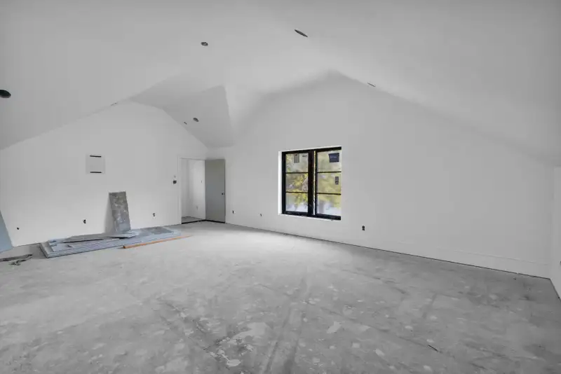 Vaulted unfinished room with white walls, a black-framed window, and a sloped ceiling.