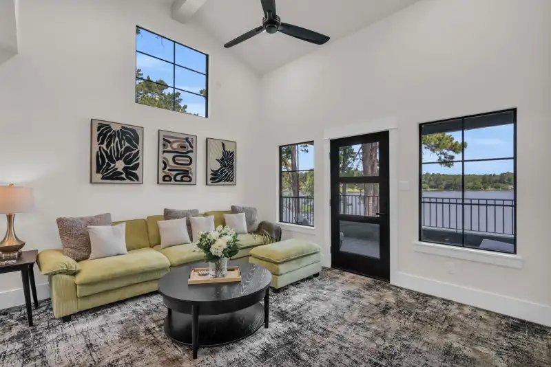 Bonus room with a green sectional, black-framed windows, and a patterned gray rug.