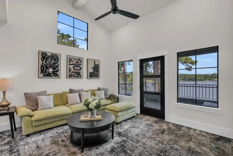 Bonus room with a green sectional, black-framed windows, and a patterned gray rug.