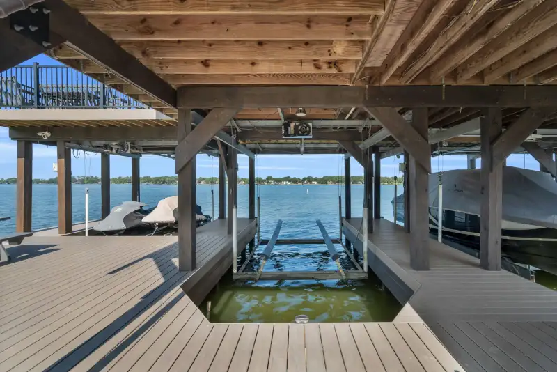Underside of a boathouse showing wood framing, a boat lift, and decking over the water.