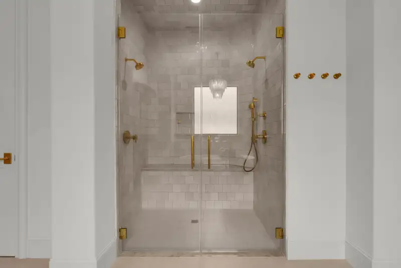 Walk-in shower with a glass door, brass hardware, and tile walls.