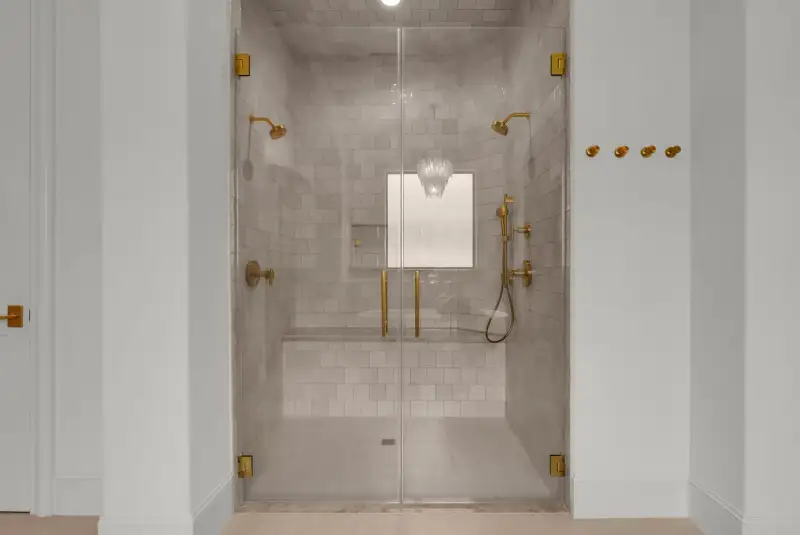 Walk-in shower with a glass door, brass hardware, and tile walls.