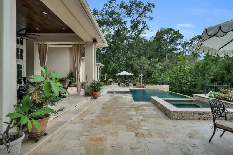 Pool deck with a rectangular pool and attached spa on travertine pavers, and a scalloped umbrella.