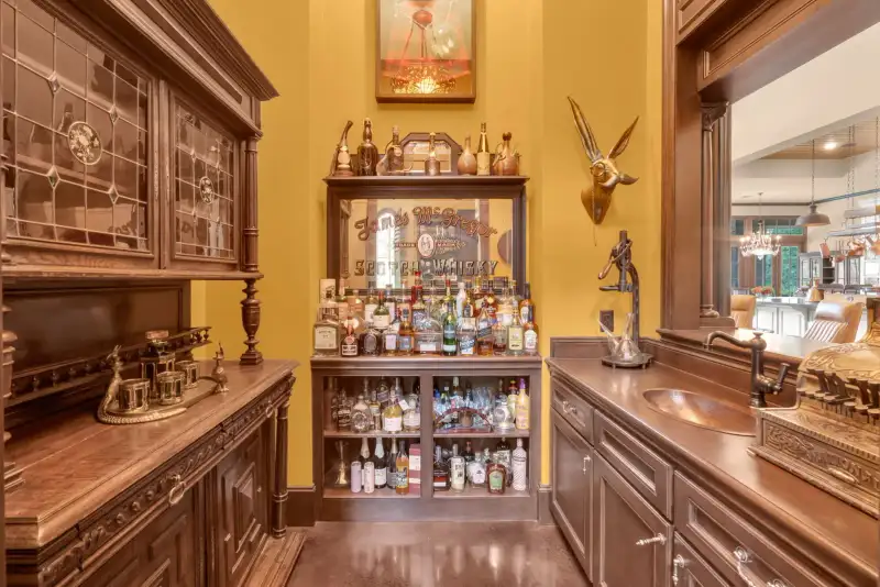 Wood bar with leaded glass cabinets, liquor bottle shelves, a copper sink, and a brass scale on the counter.
