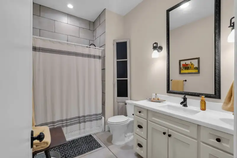 Bathroom with a tub-shower, gray tile surround, a striped shower curtain, a toilet, and a vanity with a black-framed mirror.