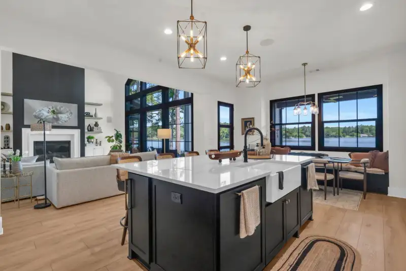 Open kitchen and living area with a dark island, pendant lights, and a fireplace wall in view.