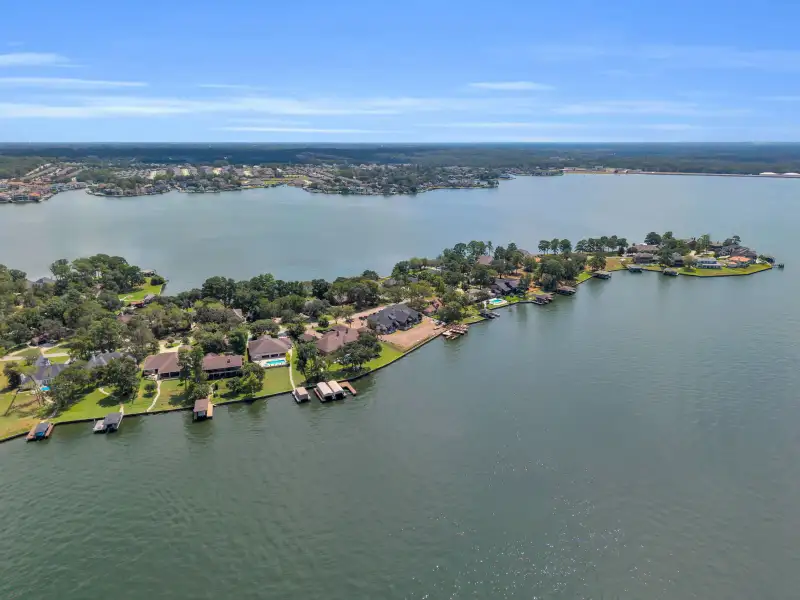 Aerial view of a tree-lined shoreline with homes, boat docks, and a wide lake beyond.