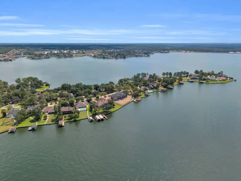 Aerial view of a tree-lined shoreline with homes, boat docks, and a wide lake beyond.