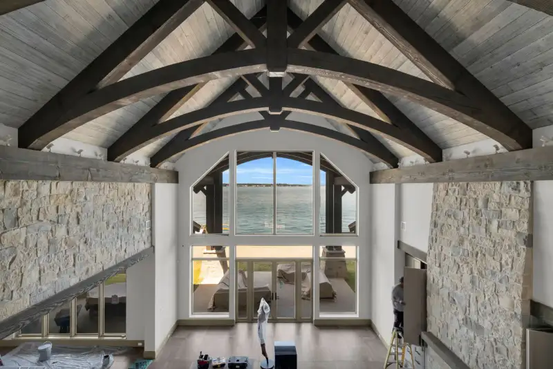 Two-story room with exposed timber trusses, tall windows, and a view of the water.