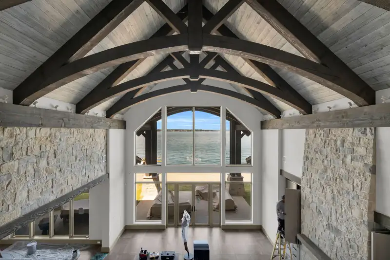 Two-story room with exposed timber trusses, tall windows, and a view of the water.