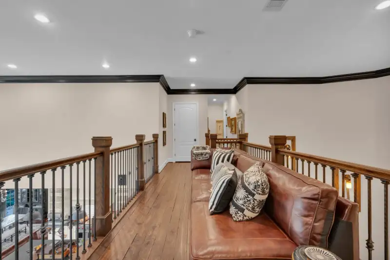 Upper landing with a brown leather sofa, striped pillows, and an iron and wood railing.