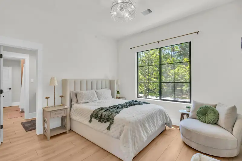 Bedroom with an upholstered bed, a tall black-framed window, and a white swivel chair.