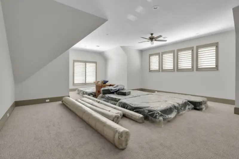 Upstairs bonus room with carpet, a ceiling fan, and stacked mattresses in plastic wrap.