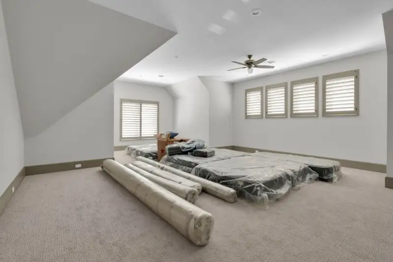 Upstairs bonus room with carpet, a ceiling fan, and stacked mattresses in plastic wrap.