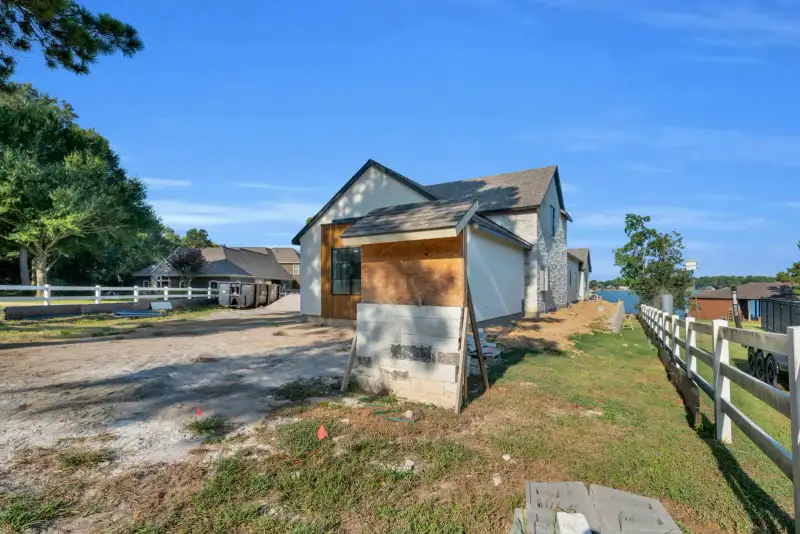Side exterior of an unfinished stucco house with a block base and a white rail fence.