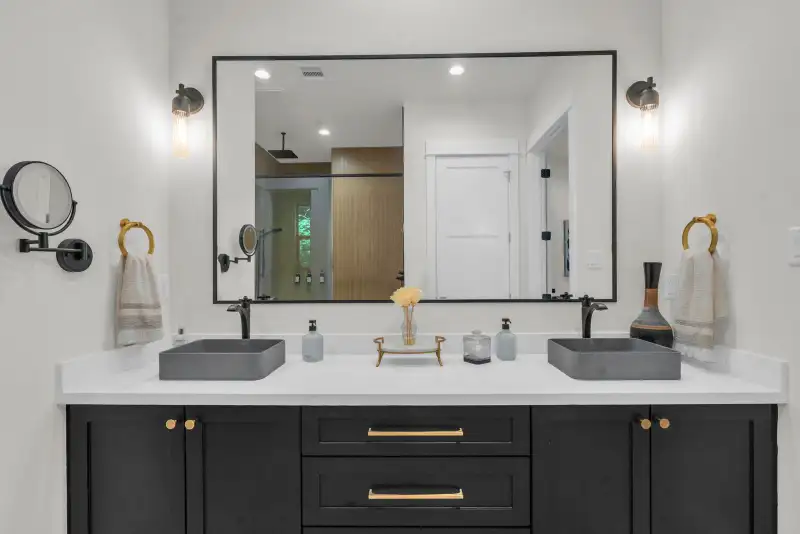 Double vanity with black cabinets, two gray vessel sinks, a framed mirror, and black wall sconces.
