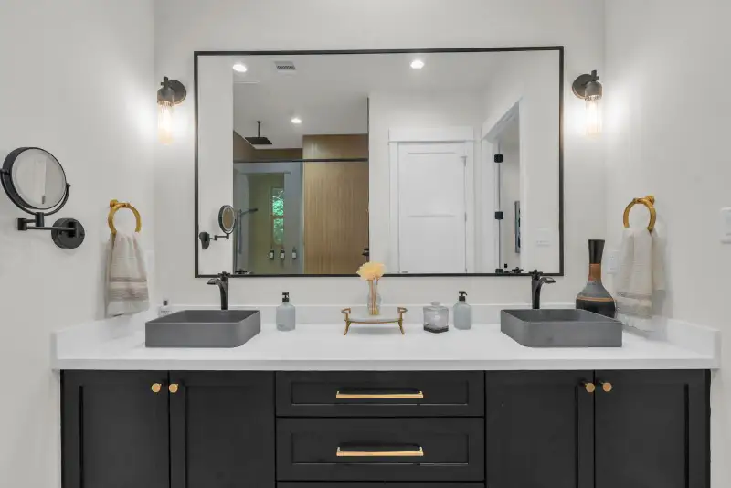 Double vanity with black cabinets, two gray vessel sinks, a framed mirror, and black wall sconces.