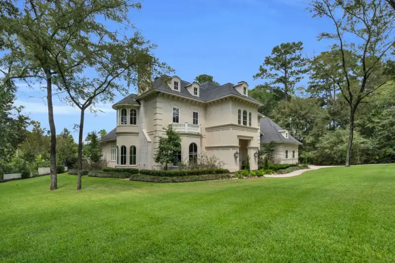 Cream stucco French-style home with arched windows, a second-floor balcony, and a gray slate roof under blue sky.