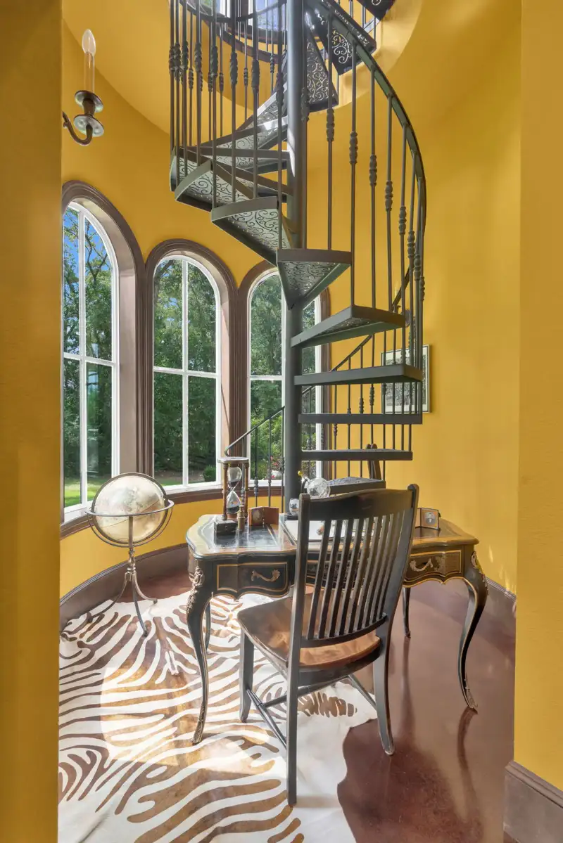 Corner with a desk, a zebra-print rug, and arched windows beside a spiral iron staircase.